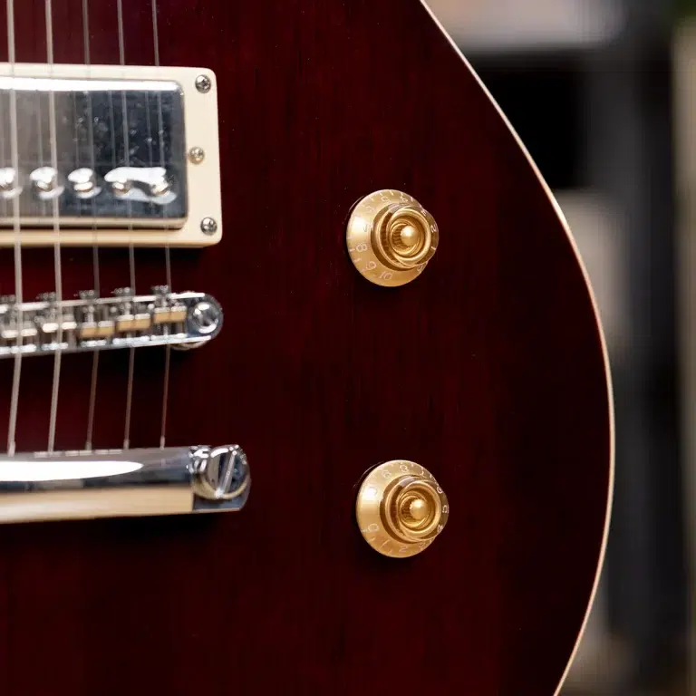 Close-up of a dark red electric guitar body with two gold control knobs and chrome hardware near the bridge and pickups. ขายราคาพิเศษ