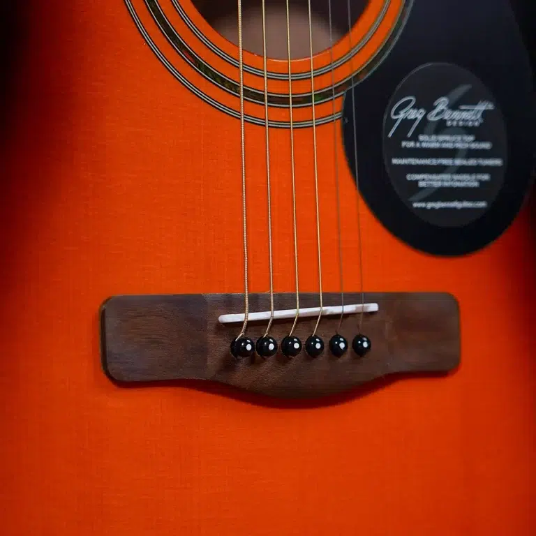 Close-up of an orange acoustic guitar showing the wooden bridge, six strings, and saddle. ขายราคาพิเศษ