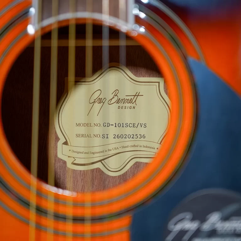 Close-up of an acoustic guitar soundhole showing the Greg Bennett Design label with model GD-101SCE/VS and serial number SI 260202536, crafted details visible. ขายราคาพิเศษ