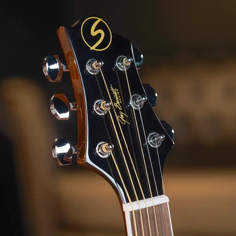 Close-up of a glossy black guitar headstock with six chrome tuning pegs and gold script branding, strings visible along the fret area. ขายราคาพิเศษ