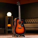 Sunburst acoustic guitar on a stand in a cozy studio with warm lighting and a tufted sofa in the background. ขายราคาพิเศษ