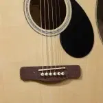 Close-up of an acoustic guitar showing the strings over the wooden bridge and round soundhole. ขายราคาพิเศษ
