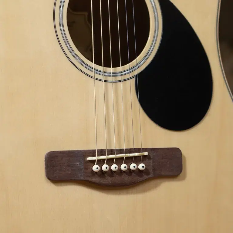Close-up of an acoustic guitar showing the strings over the wooden bridge and round soundhole. ขายราคาพิเศษ