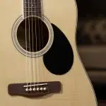 Close-up of an acoustic guitar showing the soundhole, six strings, and wooden bridge with white bridge pins on a light wood body. ขายราคาพิเศษ