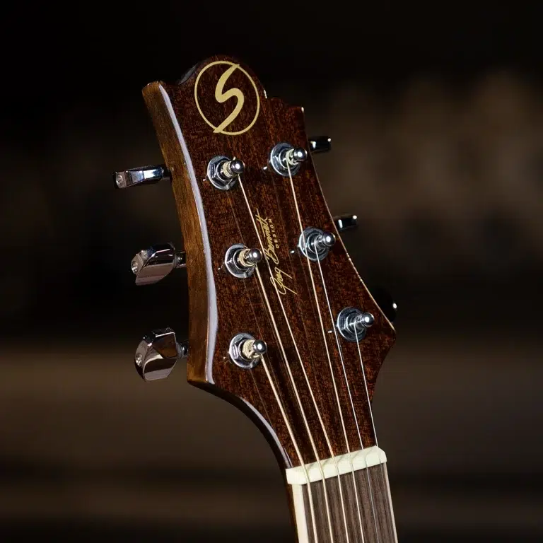 Close-up of a wooden guitar headstock with six tuning pegs and strings, showing the nut and rich wood grain. ขายราคาพิเศษ