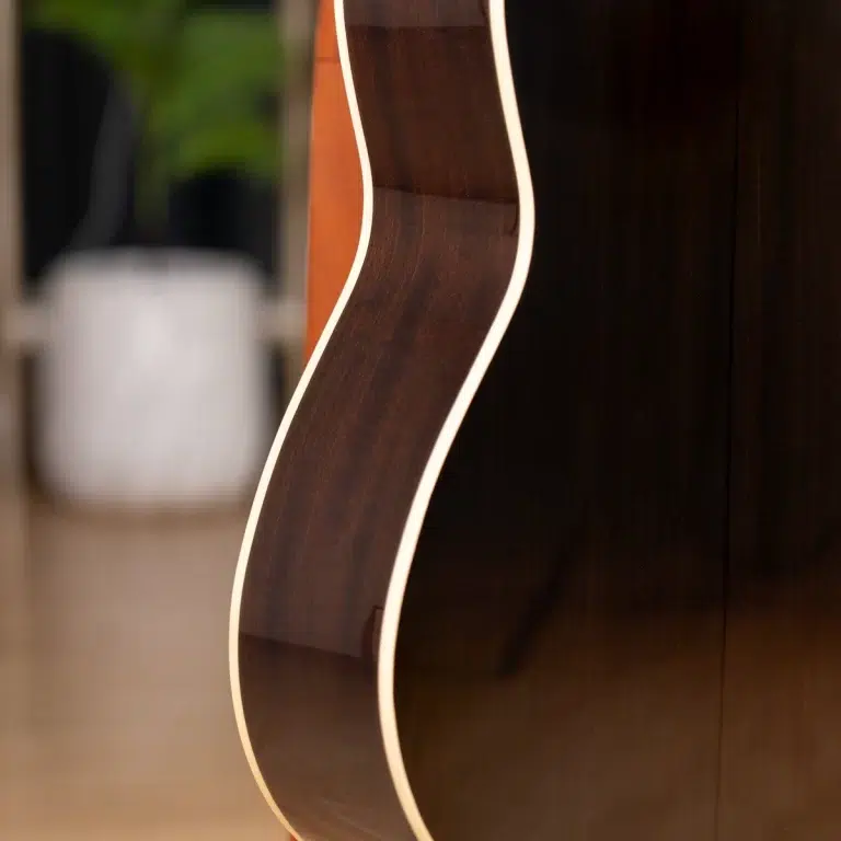 Close-up of a glossy dark brown guitar body’s curved edge with cream binding, background blurred. ขายราคาพิเศษ