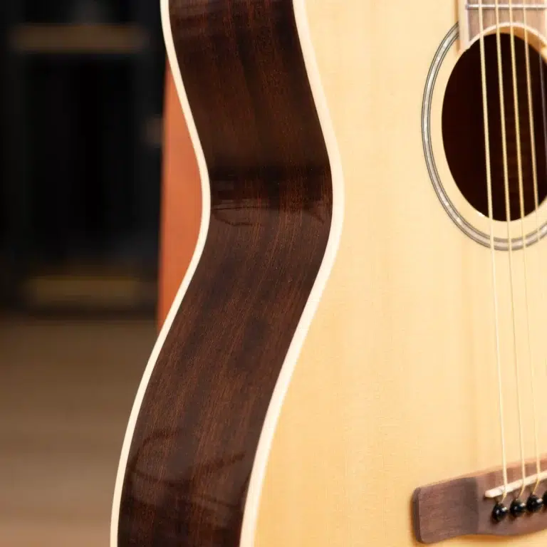 Close-up of an acoustic guitar showing the light top wood, dark side wood, and strings near the bridge by the soundhole ขายราคาพิเศษ