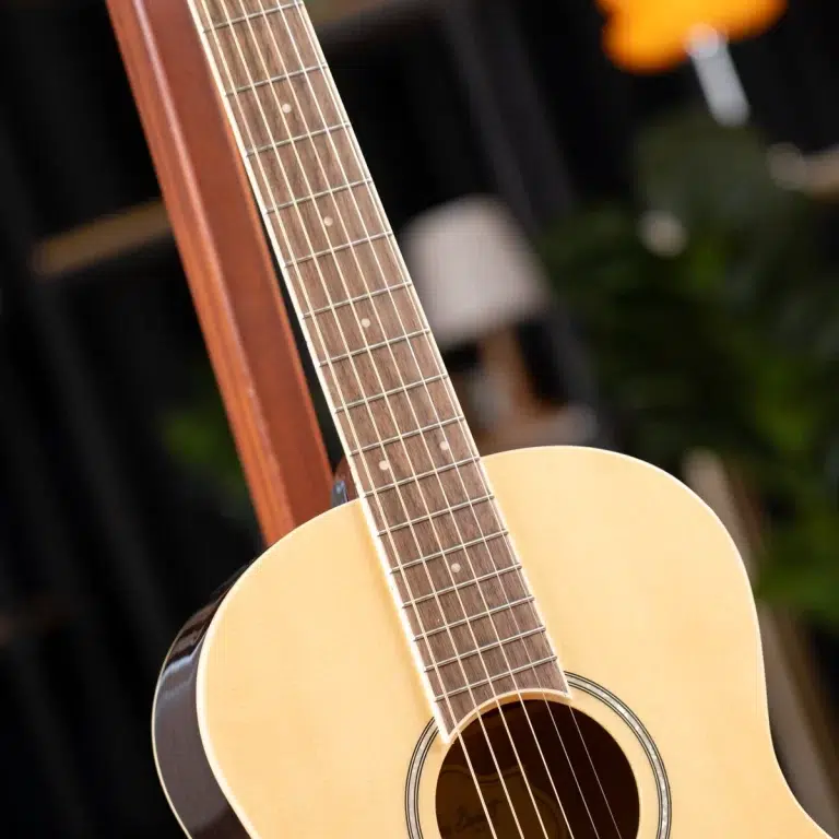 Close-up of an acoustic guitar neck and fretboard, with light-colored body visible at the bottom right. ขายราคาพิเศษ