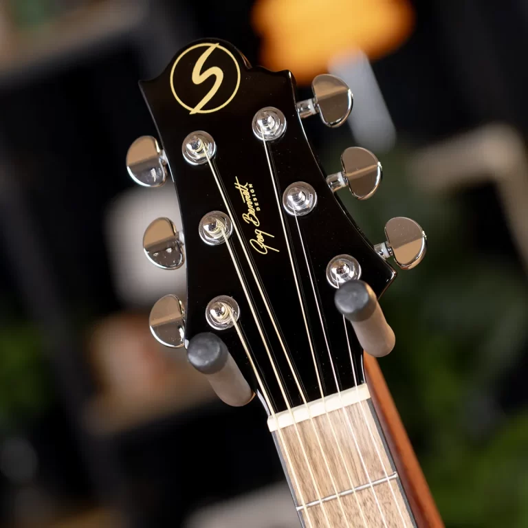 Close-up of a black guitar headstock with six chrome tuning pegs and strings, logo at the top. ขายราคาพิเศษ