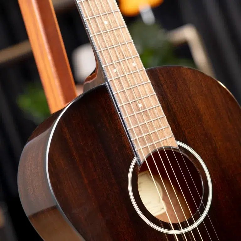 Close-up of a dark wooden acoustic guitar focusing on the neck, frets, and six strings over the sound hole. ขายราคาพิเศษ