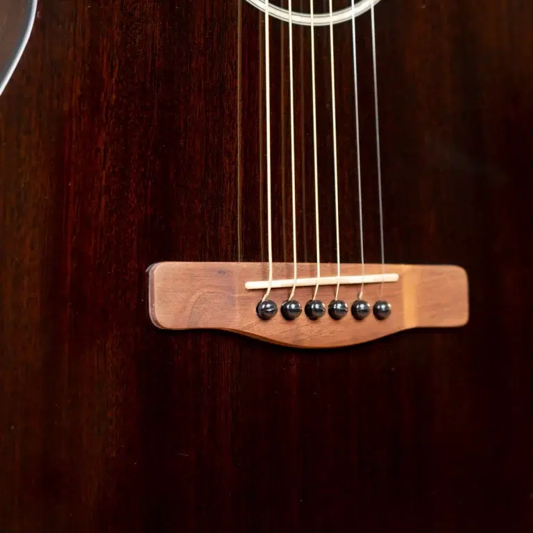 Close-up of a dark wood guitar body showing the bridge, six strings, and bridge pins on an acoustic guitar. ขายราคาพิเศษ