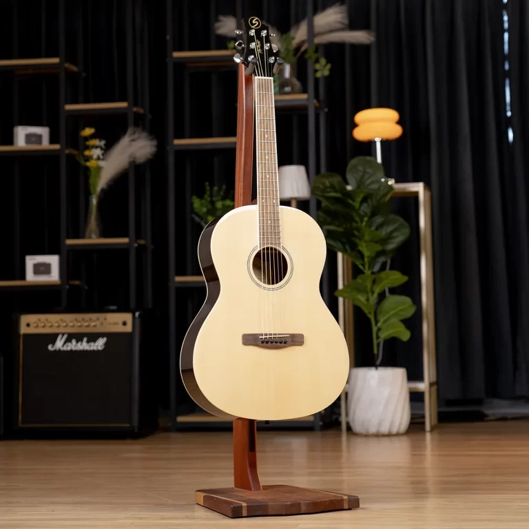 Acoustic guitar on a wooden stand in a music studio, with a Marshall amplifier and plants visible in the background. ขายราคาพิเศษ