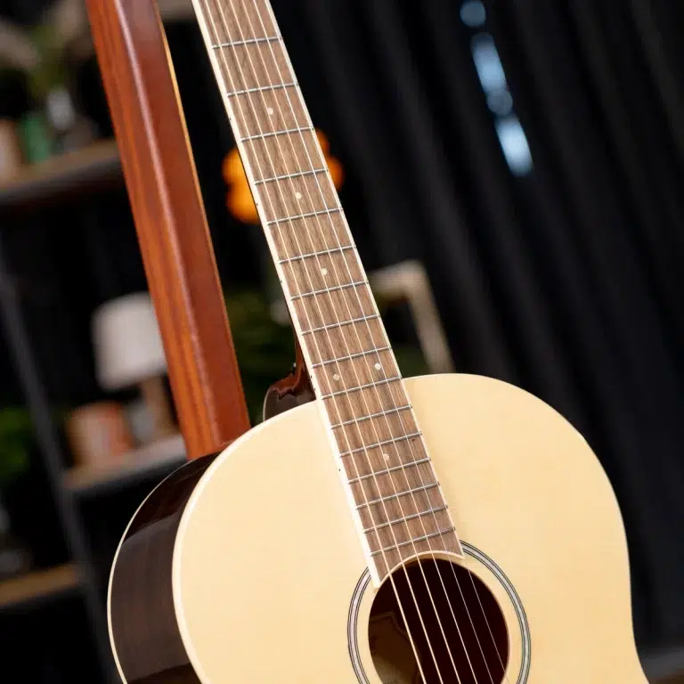 Close-up of an acoustic guitar neck and light-colored body resting on a wooden stand, strings visible in the foreground ขายราคาพิเศษ