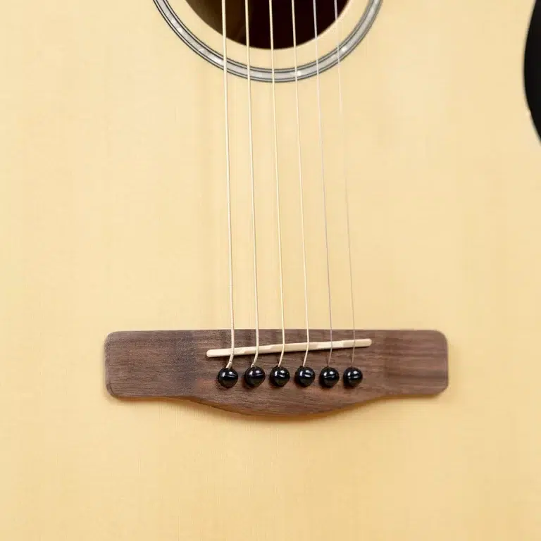 Close-up of an acoustic guitar bridge with six strings anchored by black bridge pins on a light wood body. ขายราคาพิเศษ