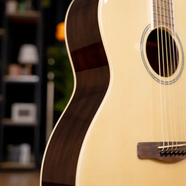 Close-up of an acoustic guitar's cream top and dark back, with strings over the sound hole in focus. ขายราคาพิเศษ