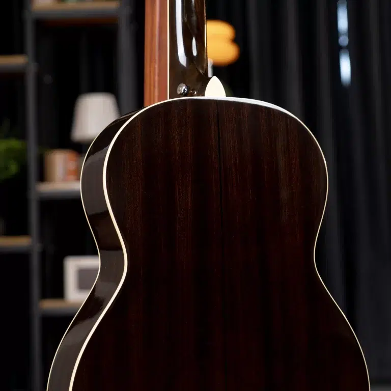 Close-up of a dark wooden acoustic guitar body with white binding, neck extending upward in a workshop setting ขายราคาพิเศษ