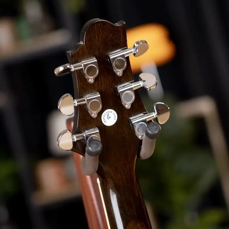Close-up of a dark wood guitar headstock with six chrome tuning pegs and a QC sticker visible on the back. ขายราคาพิเศษ