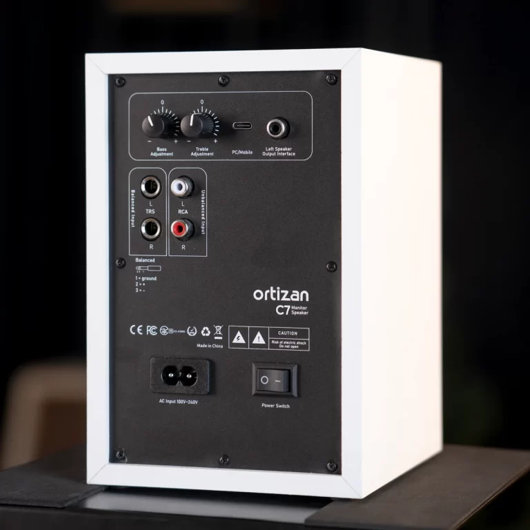 Rear panel of an Ortizan C7 monitor speaker showing balance and unbalanced inputs (RCA/TRS), control knobs for bass and treble, and power switch, on a black plate with white case edges. ขายราคาพิเศษ