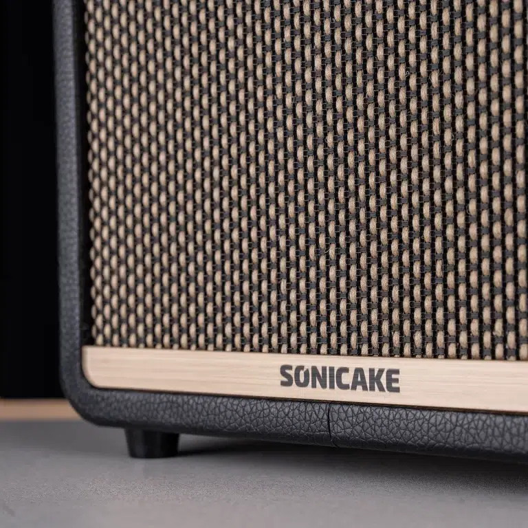 Close-up of a SONICAKE amplifier front: woven black-and-tan grille with a light wood trim. ขายราคาพิเศษ