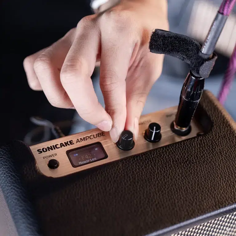 Close-up of a hand adjusting knobs on a copper SonicaKE AmpCube portable amplifier. ขายราคาพิเศษ