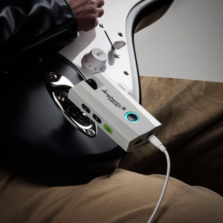 Close-up of a white USB audio interface connected to a cable, resting on a black surface with a hand adjusting a white tone knob nearby, and a blue-lit button visible on the device. ขายราคาพิเศษ