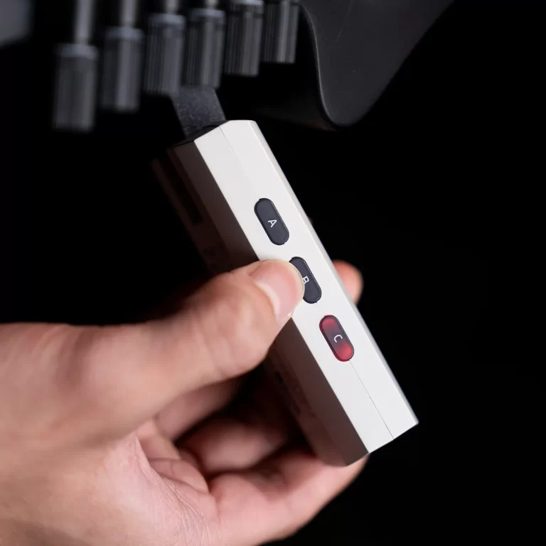 Hand holding a small white device with black A and B buttons and a red C button, against a dark background. ขายราคาพิเศษ