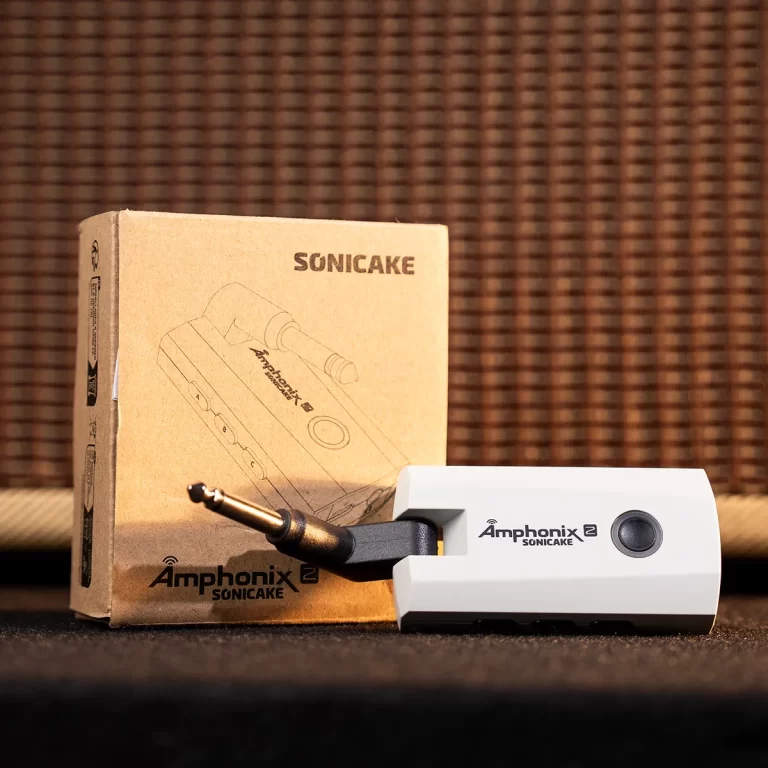 Amphonix Sonicake device (white) with plug inserted, placed beside its brown packaging box on a dark surface. ขายราคาพิเศษ