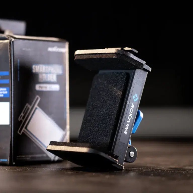 Close-up of a black plastic device with foam padding and a blue lever, resting against its packaging box on a dark surface. ขายราคาพิเศษ