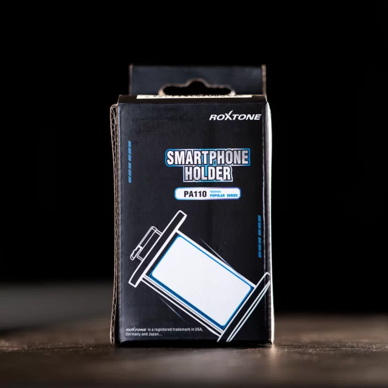 Box packaging for a Roxtone PA110 smartphone holder, black with blue/white graphics on a dark surface ขายราคาพิเศษ