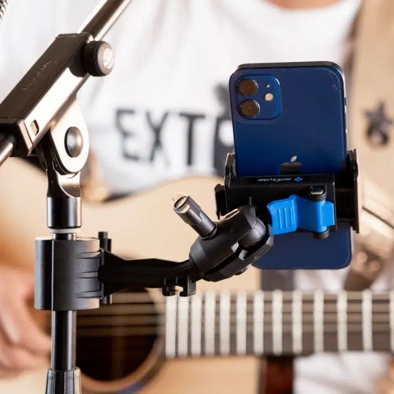 Blue iPhone secured in a clamp on a tripod-mounted gimbal, guitar in the blurred background. ขายราคาพิเศษ