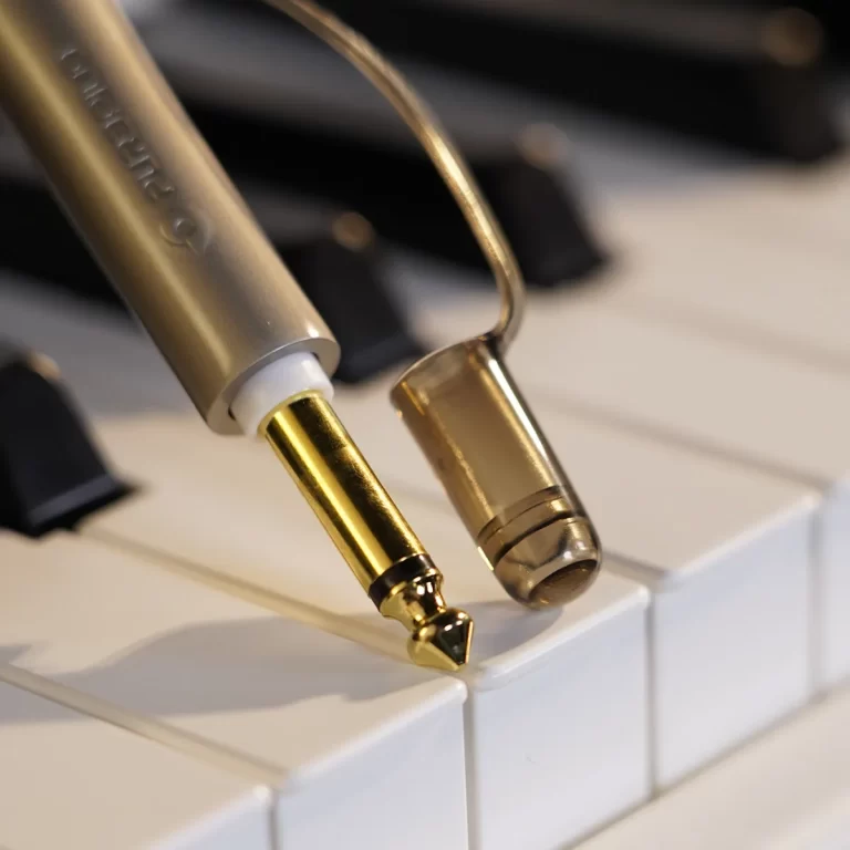 Close-up of a gold-plated audio jack resting on a white piano keyboard. ขายราคาพิเศษ