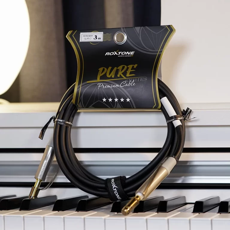 Black audio cables with gold-plated connectors coiled on a piano, Roxtone packaging in the background. ขายราคาพิเศษ