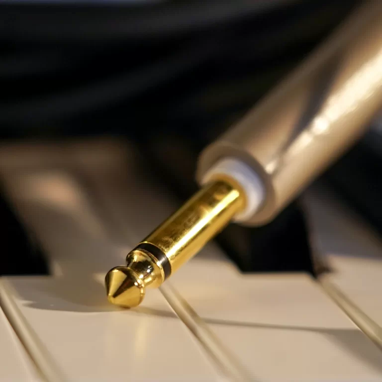 Close-up of a gold 1/4-inch audio plug resting on white piano keys. ขายราคาพิเศษ