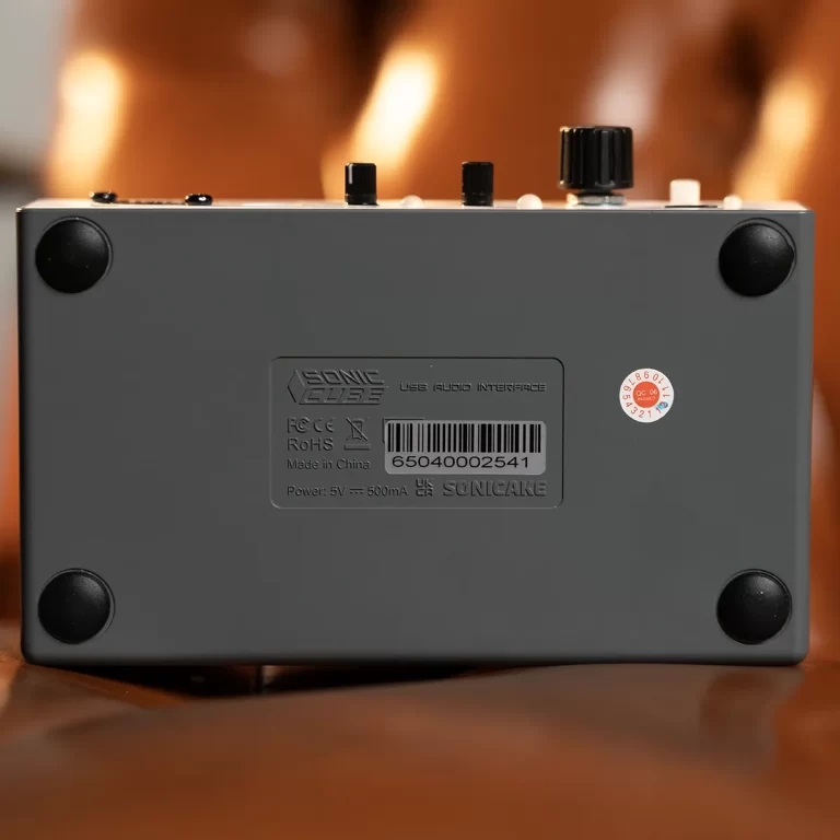Bottom view of a gray USB audio interface resting on a brown surface, showing four rubber feet and a recessed label with model and power info ขายราคาพิเศษ
