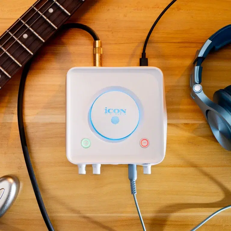 White compact audio interface with a blue LED ring, on a wooden desk, connected to a guitar cable and headphones nearby. ขายราคาพิเศษ