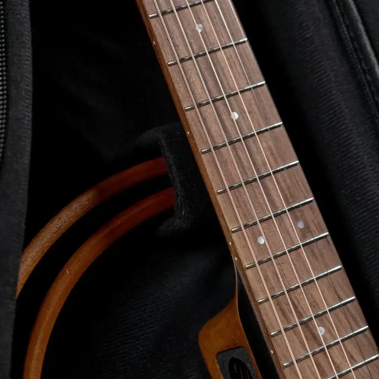 Close-up of a wooden guitar neck with metal frets and strings against a dark fabric background. ขายราคาพิเศษ