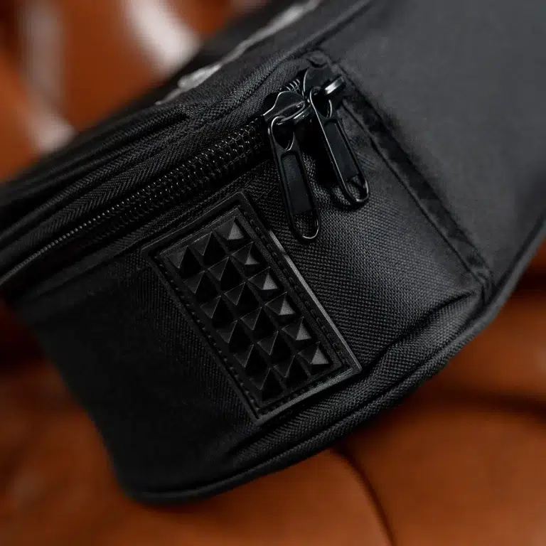 Close-up of a black bag corner with dual zipper pulls and a textured studded patch on the fabric. ขายราคาพิเศษ