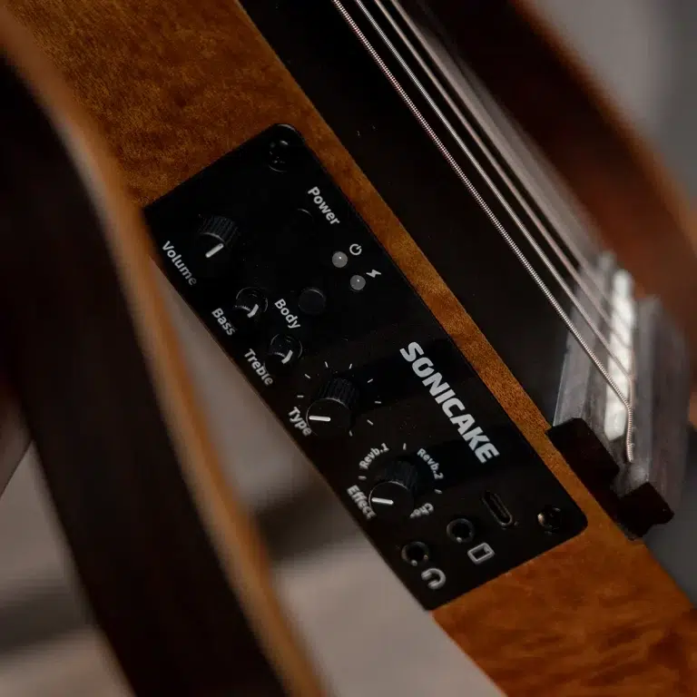 Close-up of a Sonicake guitar control panel mounted on a wooden guitar body, showing volume, bass, treble knobs and power switch on the black plate. ขายราคาพิเศษ