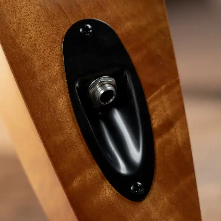 Close-up of a guitar output jack mounted in a brown wooden body, with a silver threaded connector inside a black oval plate. ขายราคาพิเศษ