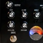 Close-up of guitar amplifier panel with knobs for Bass, Lo-Mid, Middle, Drive Level, and Drive Gain, plus a VU meter on the right side ขายราคาพิเศษ