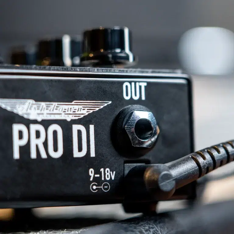 Close-up of a Pro DI guitar pedal showing the OUT jack and power input on a black metal case with a winged logo. ขายราคาพิเศษ
