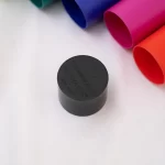 Close-up of a black plastic tube cap with embossed text placed on a white surface, colorful rolled papers in the background. ขายราคาพิเศษ