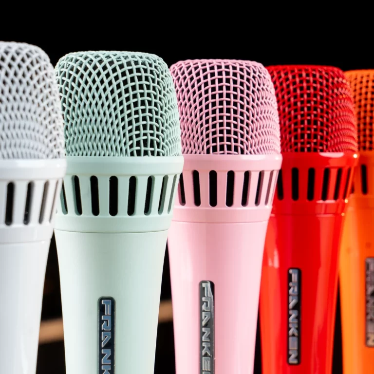 Row of colorful microphones in pastel and bright hues against a black background, shown from the mesh heads downward into the stands. ขายราคาพิเศษ