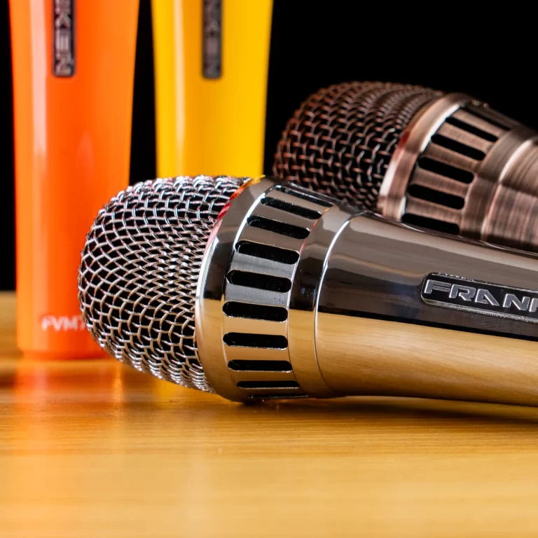 Close-up of two metal microphones on a wooden table with orange and yellow pencils in the background. ขายราคาพิเศษ