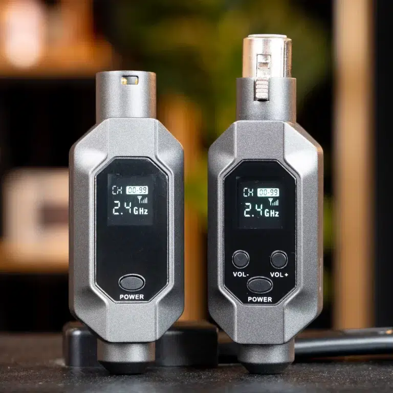 Two gray handheld wireless transmitters/receivers side by side, each with a small display showing 2.4 GHz and channel info, plus power and volume buttons. ขายราคาพิเศษ