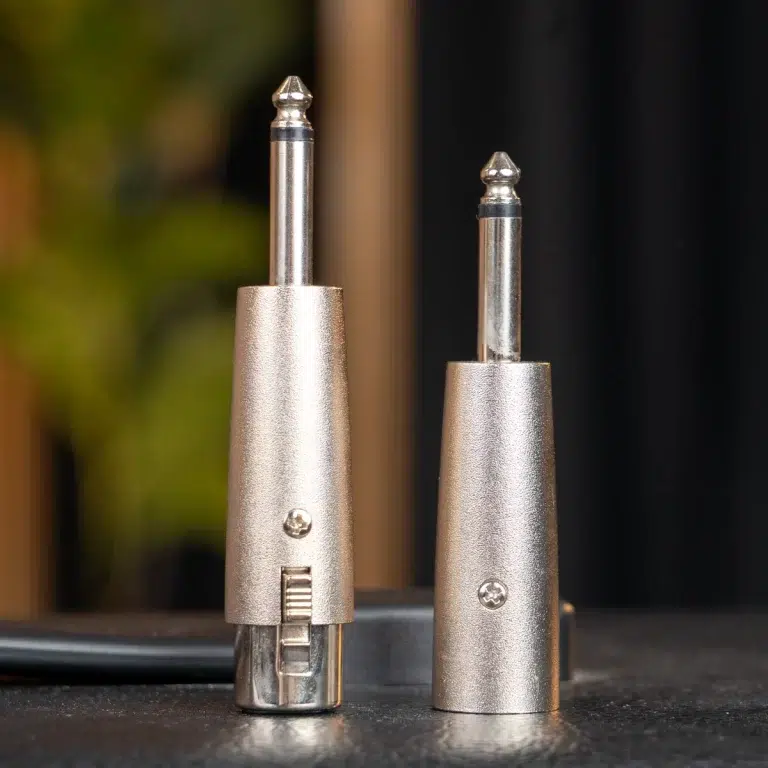 Close-up of two silver metal connector plugs standing upright on a dark surface; left plug has a small lever, right plug is shorter and smoother. ขายราคาพิเศษ