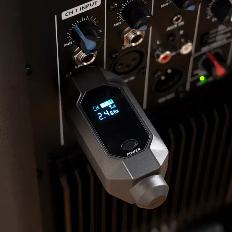 Close-up of a wireless microphone receiver showing 2.4 GHz on the blue-lit display, connected to a rack of audio inputs labeled CH1 INPUT. ขายราคาพิเศษ