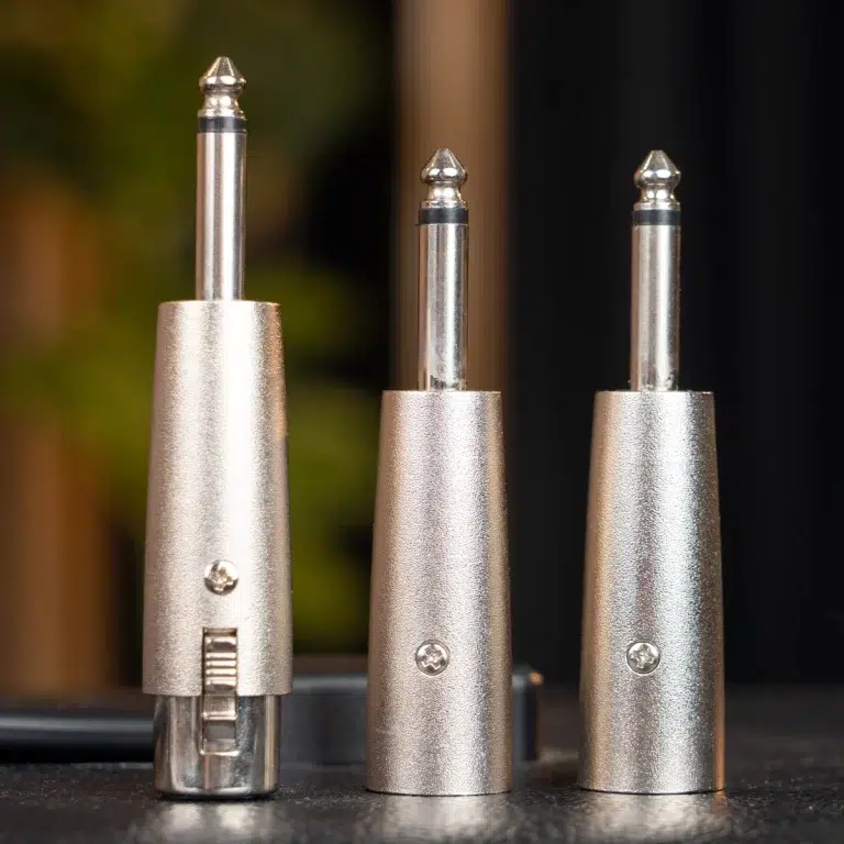 Three metal plug adapters with textured bases standing upright on a dark surface. ขายราคาพิเศษ