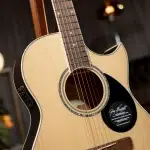 Close-up of an acoustic guitar showing the sound hole, strings, and fretboard with a cutaway body edge in warm lighting. ขายราคาพิเศษ