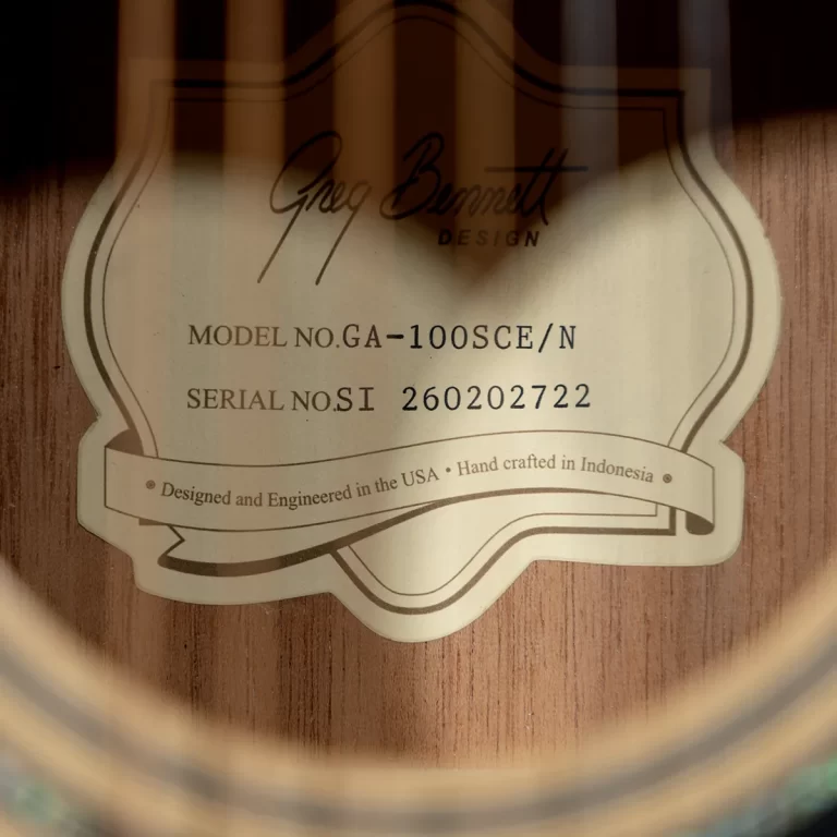 Close-up of a guitar label inside the soundhole: Greg Bennett Design, model GA-100SC/E/N, serial 260202722, designed and engineered in the USA, handmade in Indonesia. ขายราคาพิเศษ